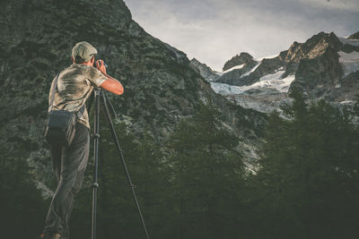 Rear view of man standing on rock against mountains