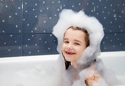 Portrait of smiling girl covered with soap sud in bathtub