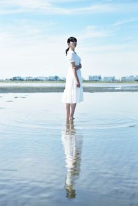 Full length of young woman standing in sea against sky