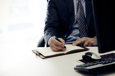 Midsection of businessman writing on book in office