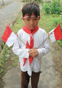 Boy holding red umbrella against trees