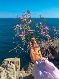 Midsection of person holding flowering plant by sea against sky