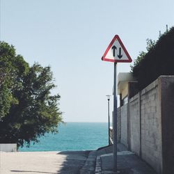 Road sign by sea against clear sky