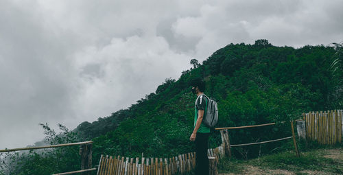 Side view of man standing by railing against sky