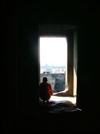 Rear view of monk crouching in doorway