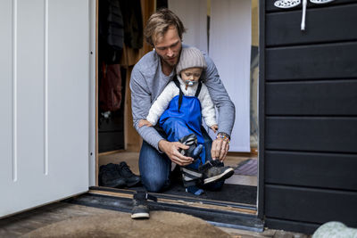 Mid adult man helping son put on shoe at doorway