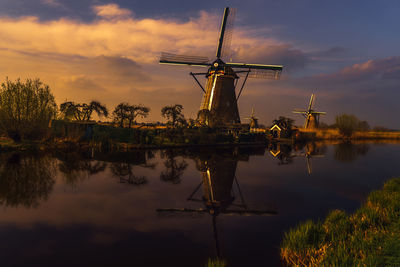 Traditional windmill by lake against sky during sunset