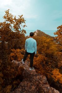 Rear view of man standing on rock against sky