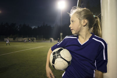 Girl holding soccer ball standing by goal post on field