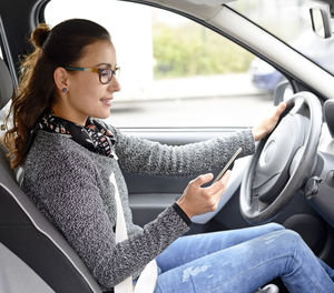 Side view of young woman using phone while sitting in car