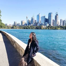 Woman by sea against modern buildings in city