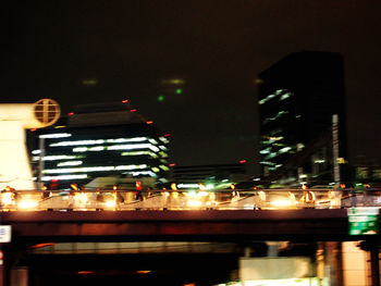 Illuminated buildings by road against sky at night