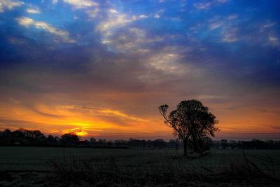 Scenic view of landscape against cloudy sky at sunset