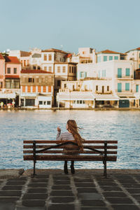 Woman sitting on bench by canal against sky