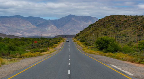 Empty road amidst mountains against sky