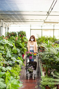 Female entrepreneur wearing face mask collecting flower while standing at garden center
