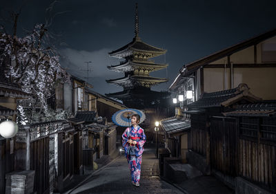Full length of woman standing against illuminated buildings at night
