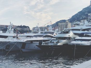 Boats moored in harbor by buildings against sky