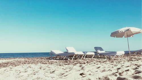 Deck chairs on beach against clear blue sky