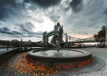 Statue of bridge over river against cloudy sky