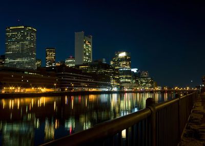 Illuminated buildings by river against sky at night