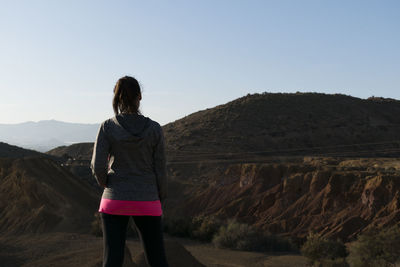 Rear view of woman standing on mountain against clear sky