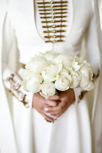 A girl in a wedding national caucasian dress holds a wedding bouquet of white peonies