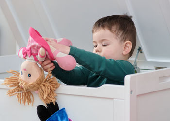 Little toddler playing with his plush toys inside the toy box