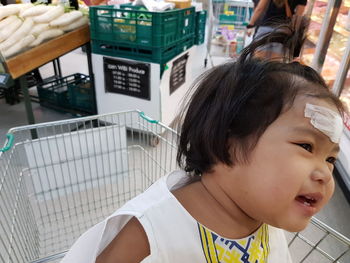 Close-up of cute girl sitting on shopping cart in supermarket