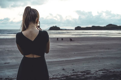 Rear view of young woman taking pictures of kangaroos at beach