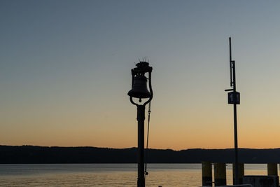 Silhouette street light by sea against clear sky