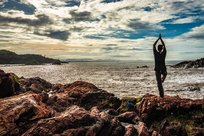 Rear view of person on rock at beach against sky