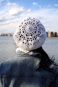 Rear view of woman wearing knit hat standing by river against sky