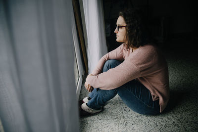 Woman with glasses sitting on the floor looking out the window