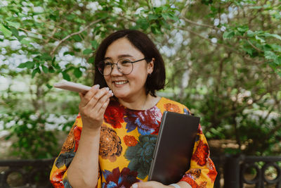 Happy woman chatting on the phone holding a laptop walking in the park