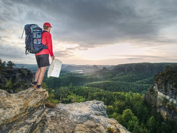 Man standing on rock looking at mountain against sky