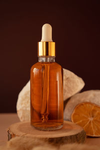 Transparent glass cosmetic dropper standing on wooden podium near stones and dry flowers 