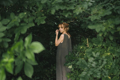 A woman stands in a dress in dense foliage