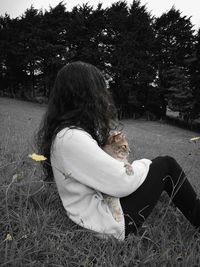 Young woman sitting on grass against trees