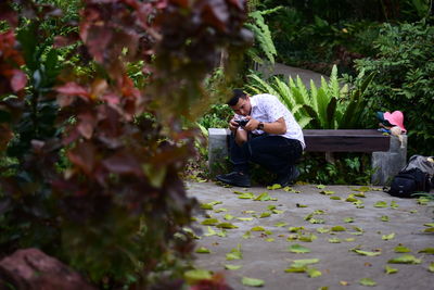 Rear view of man photographing while sitting on plant