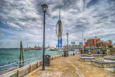 City street by sea against cloudy sky