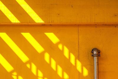 Close-up of cropped railing and sunlight on yellow wall