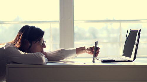 Lazy woman, office worker wearing headphones, playing mobile games with smartphone during work hours