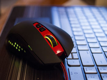 Close-up of red and black computer mouse on laptop keyboard on table