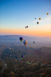 Hot air balloons flying over landscape against sky during sunset