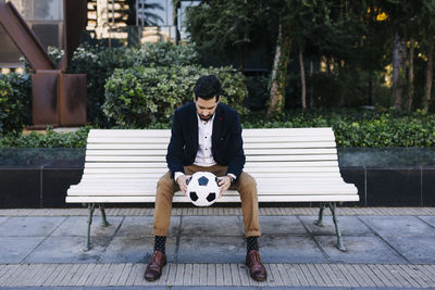 Full length portrait of young man sitting on bench