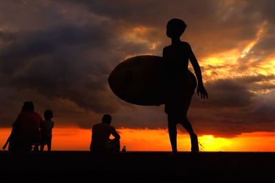 Silhouette of men against cloudy sky during sunset