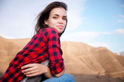 Portrait of beautiful young woman sitting against sky