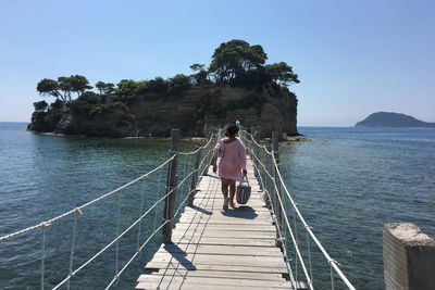 Rear view of woman walking on footbridge over sea