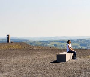 Woman sitting on land against clear sky
